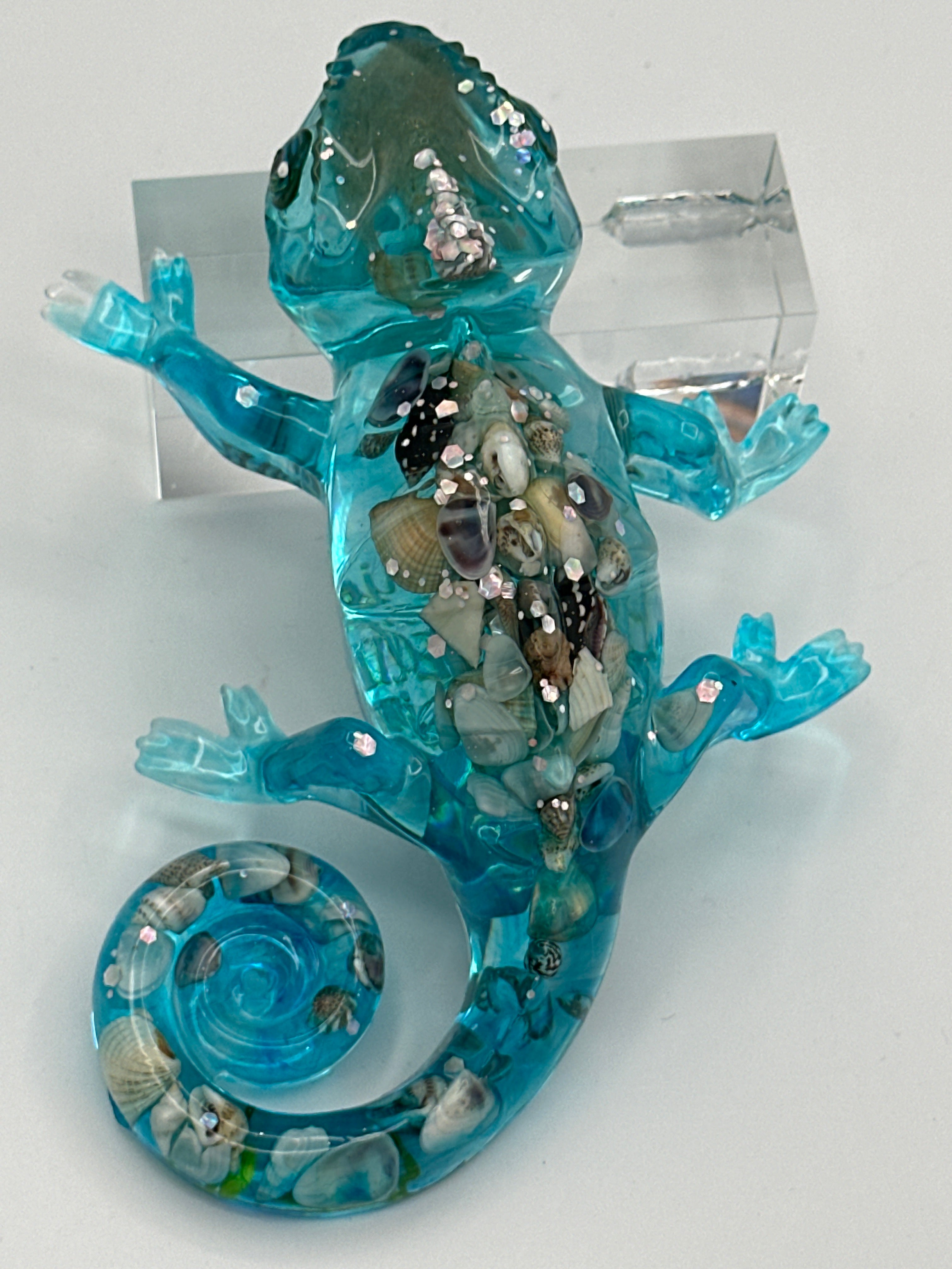 A translucent blue glass gecko sculpture filled with small seashells and clear rhinestones.